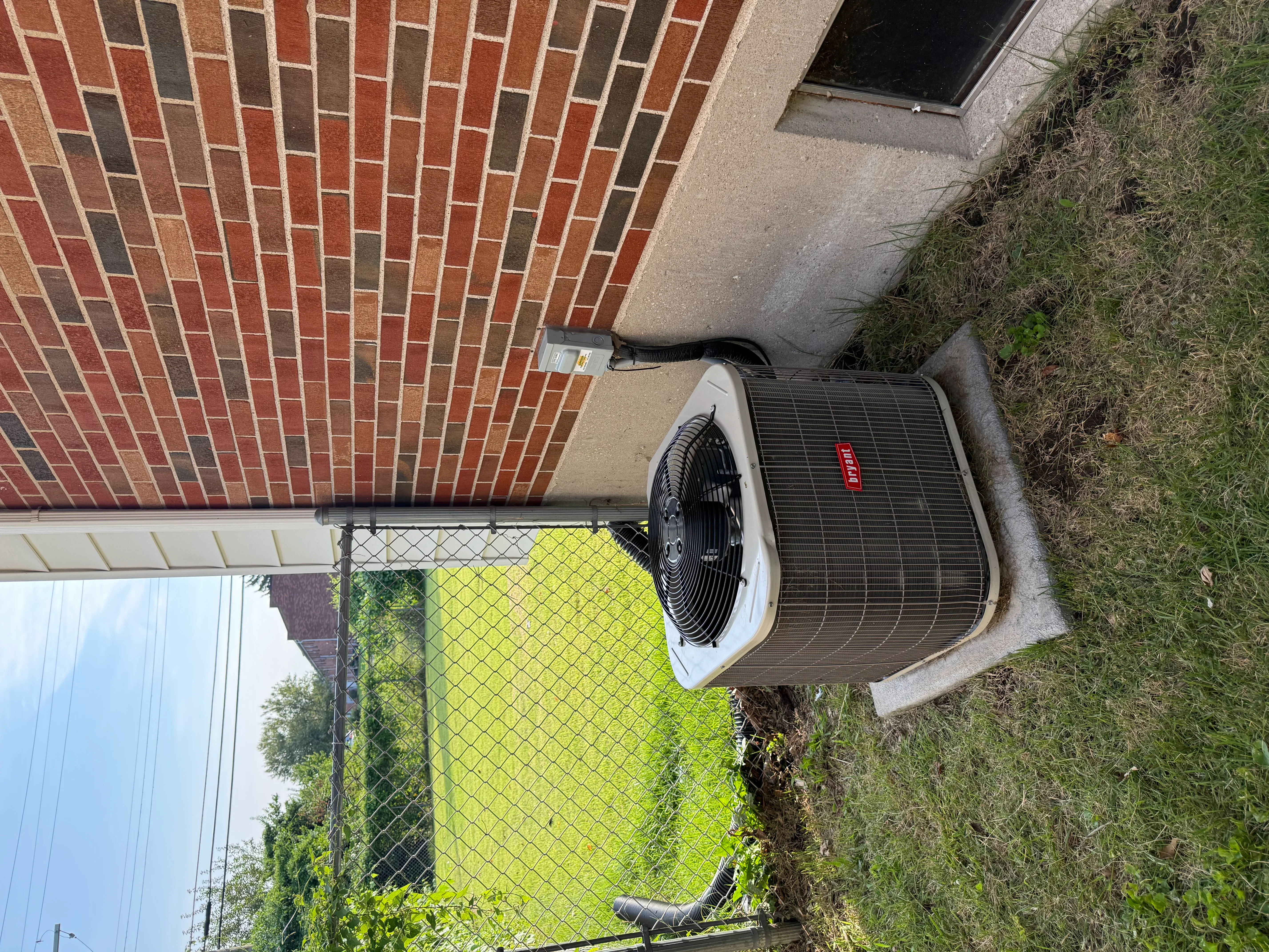 New AC condenser unit installed on concrete pad with protective chain-link fence enclosure
