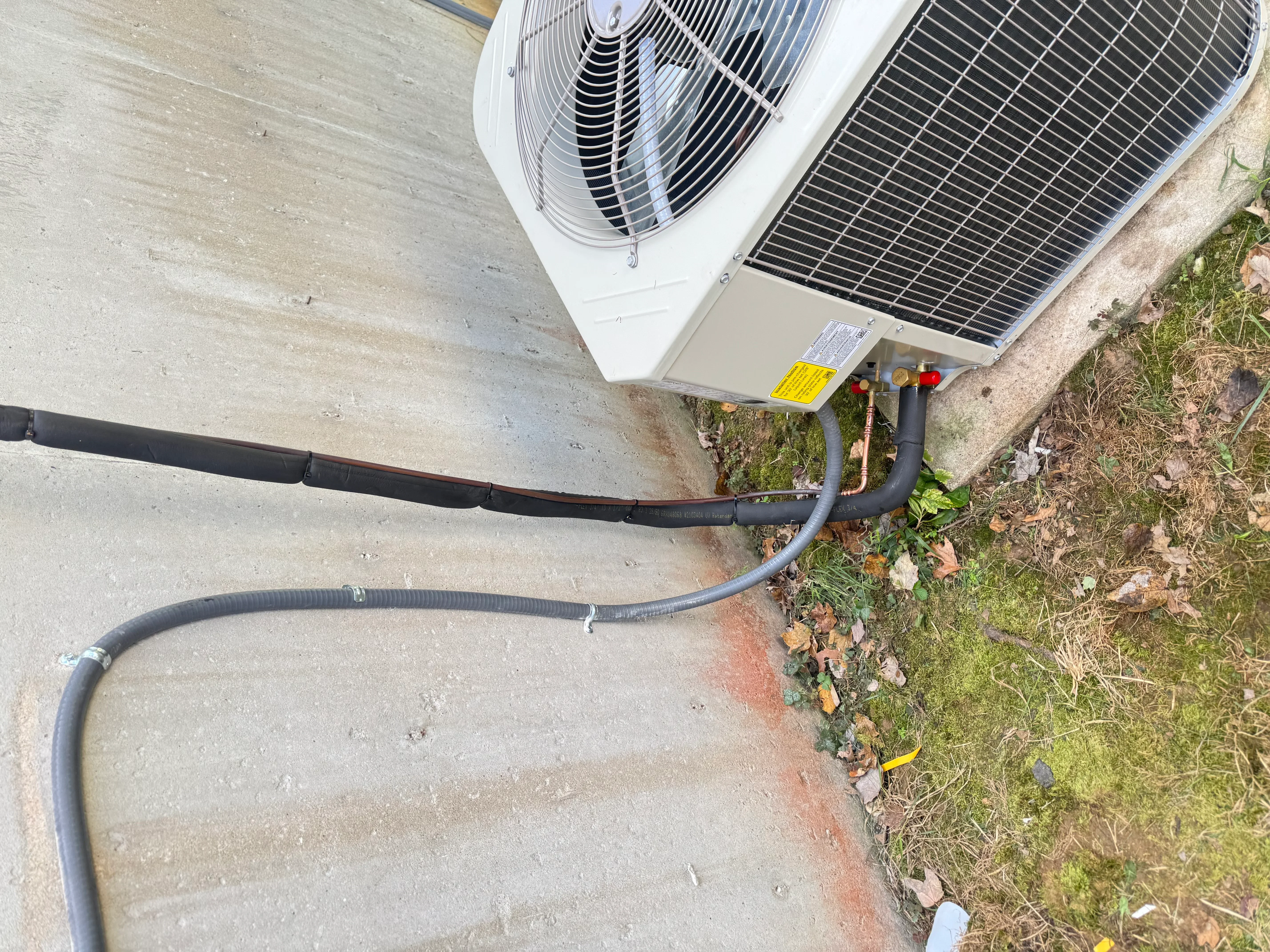 Heat pump outdoor unit with black refrigerant lines and condensate drain installation