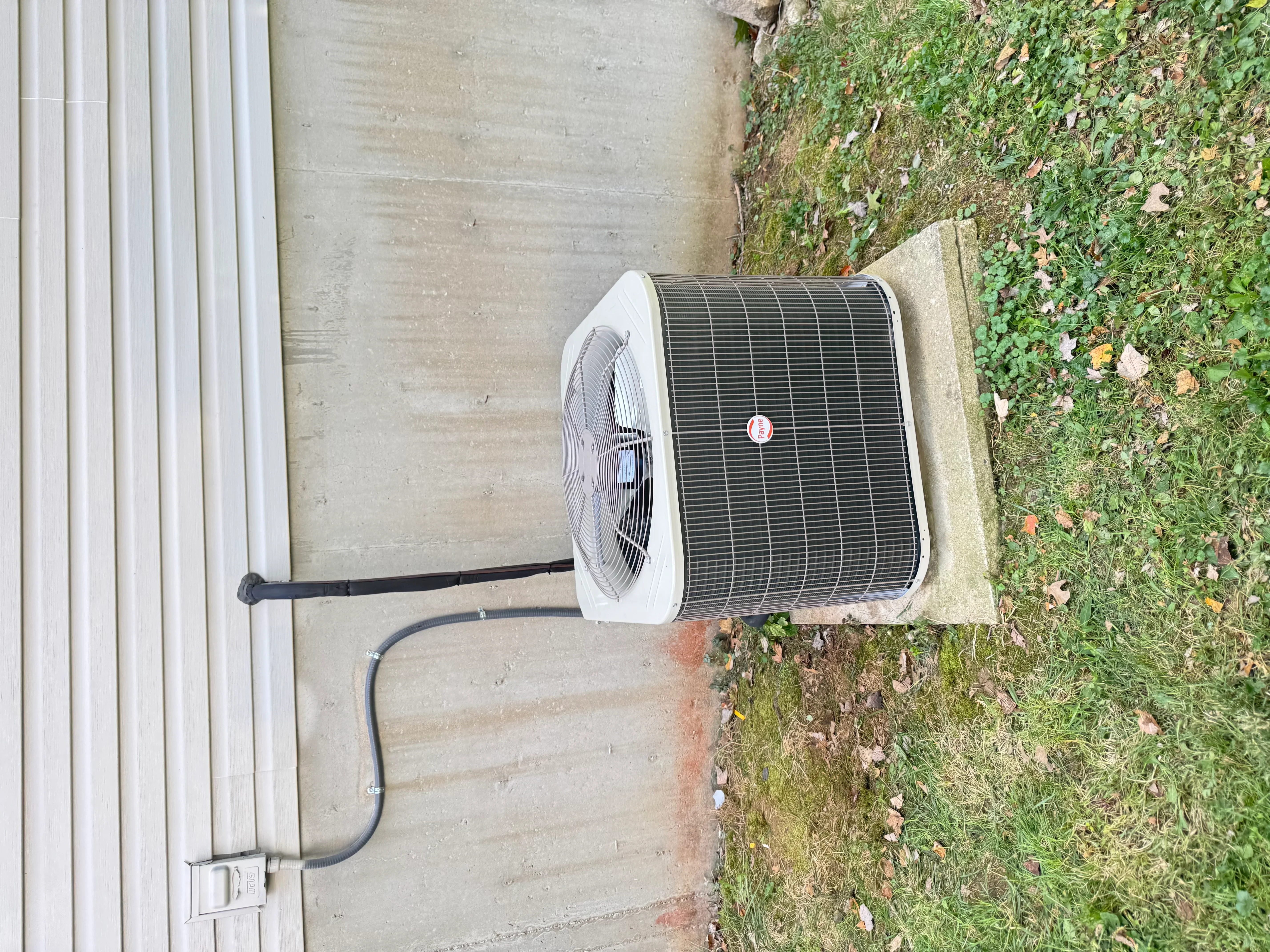 White AC condenser unit with aluminum fins installed on concrete pad with refrigerant lines