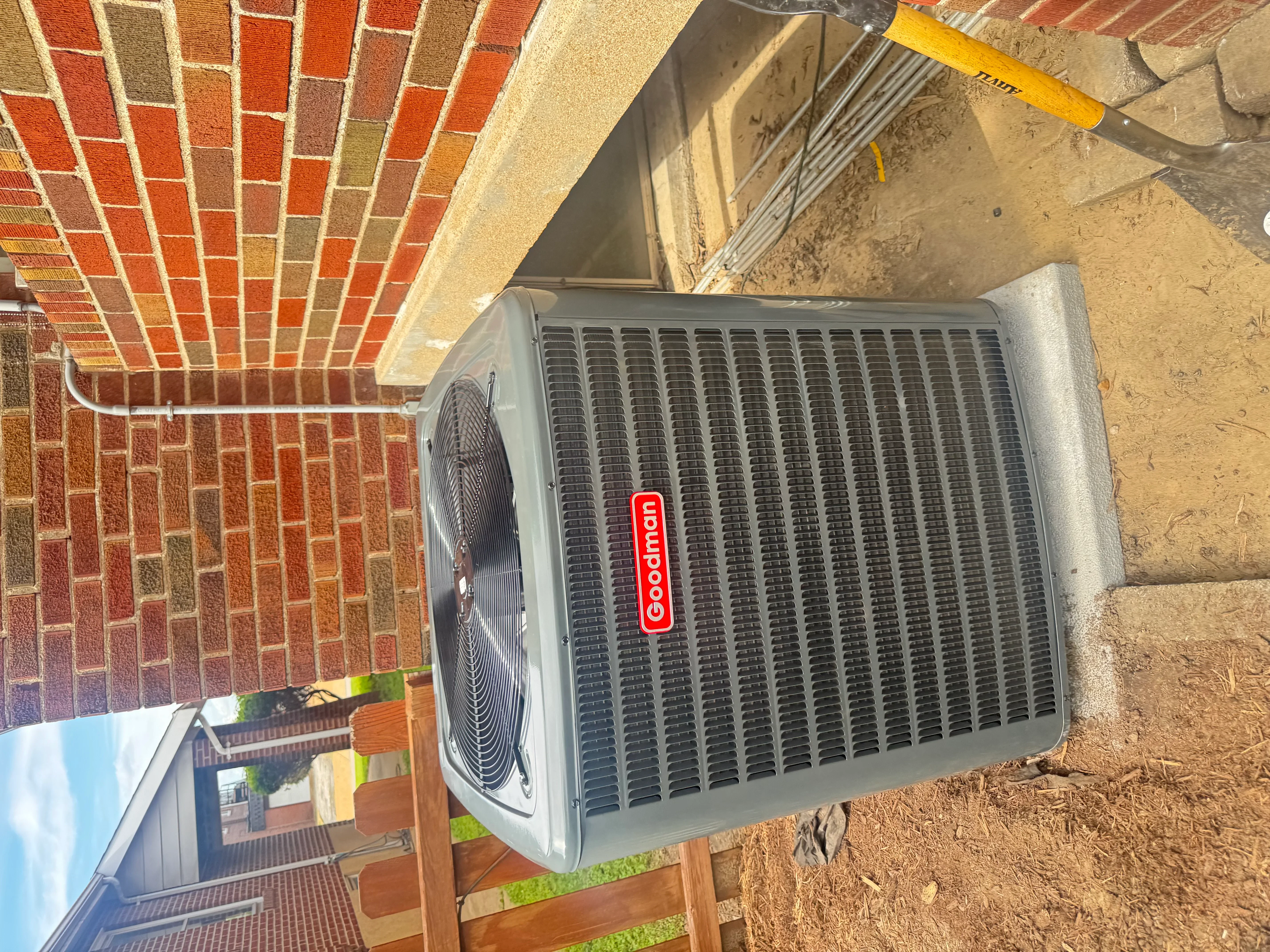 Goodman AC condenser unit installed on concrete pad next to brick home exterior