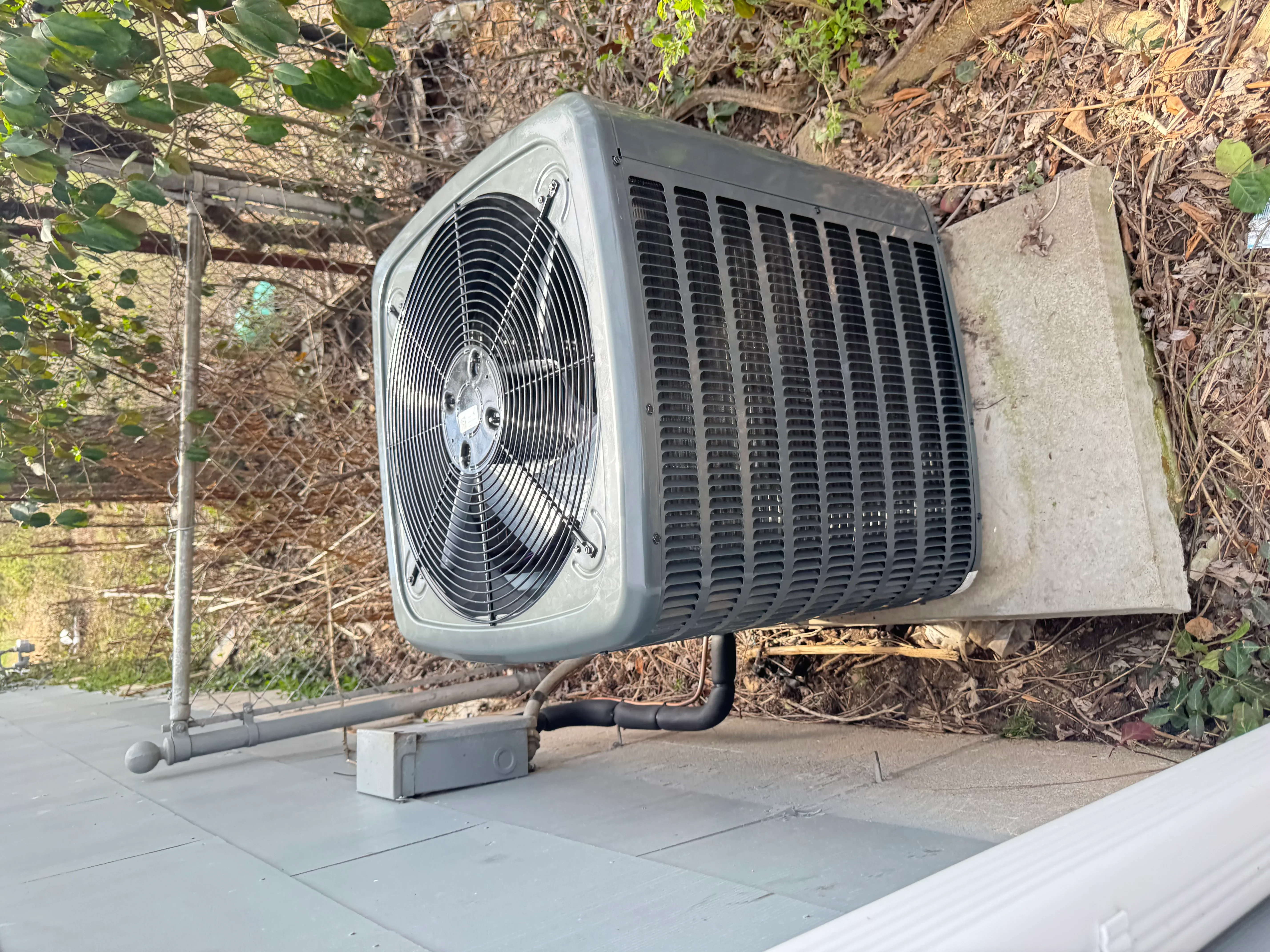 Installed AC condenser unit on concrete pad with electrical disconnect and refrigerant lines