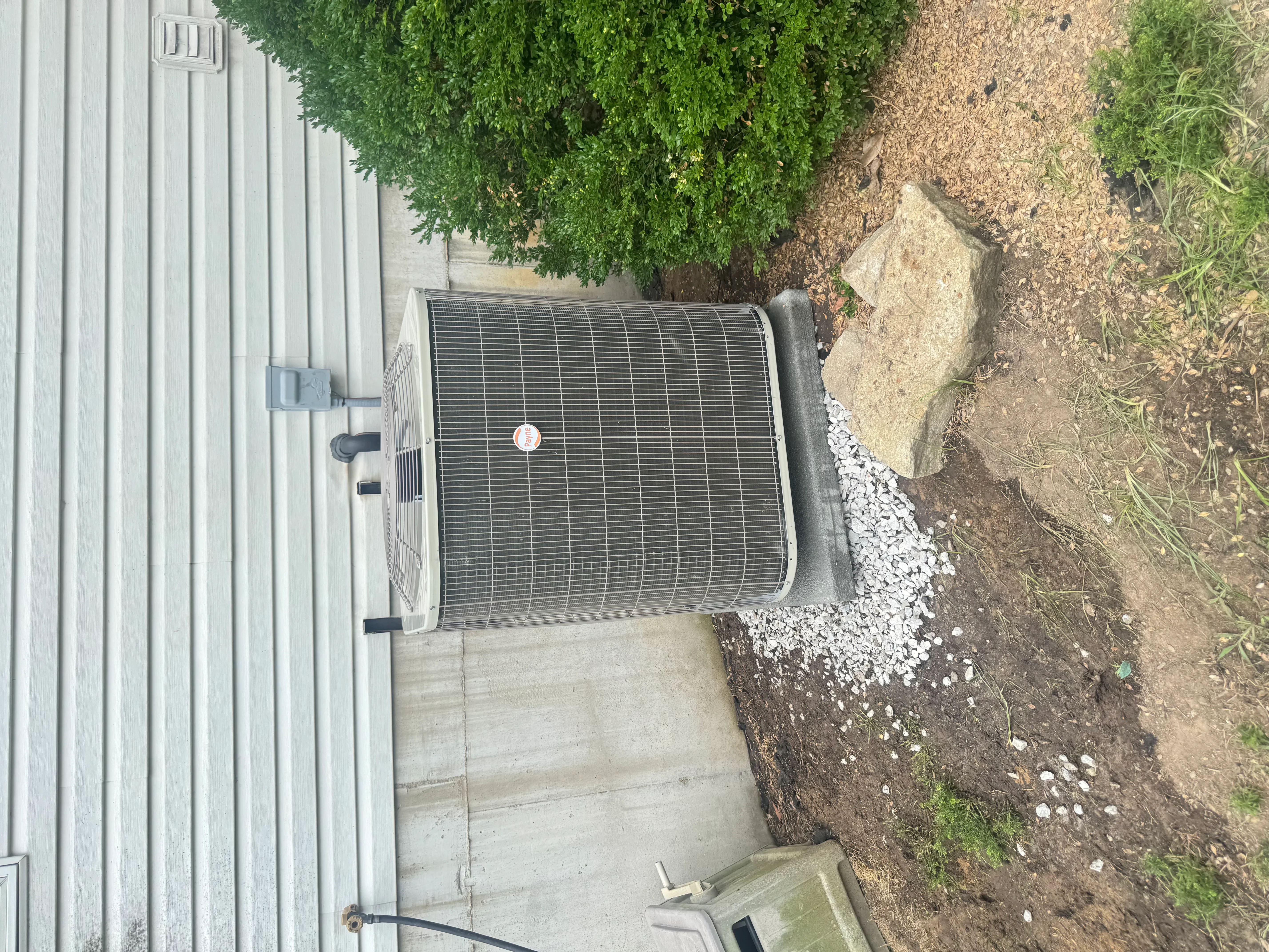 AC condenser unit installed on concrete pad with gravel base and metal building exterior